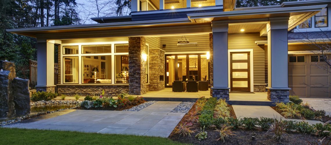 Luxurious new construction home exterior with front patio and column porch. Outdoor living space boasts taupe wicker chairs facing a stone outdoor fireplace. Northwest, USA